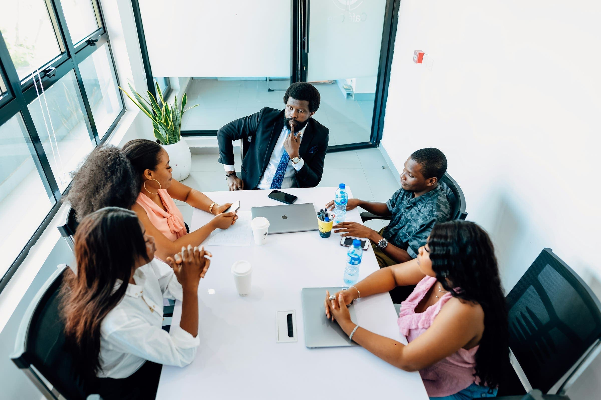 Business team meets around a white boardroom table led by a man in a suit