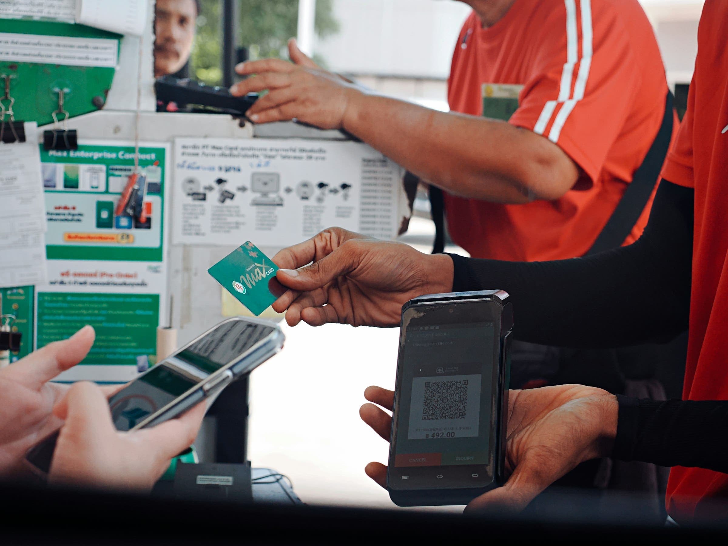 Customer holds a smartphone near a terminal displaying a QR code at checkout