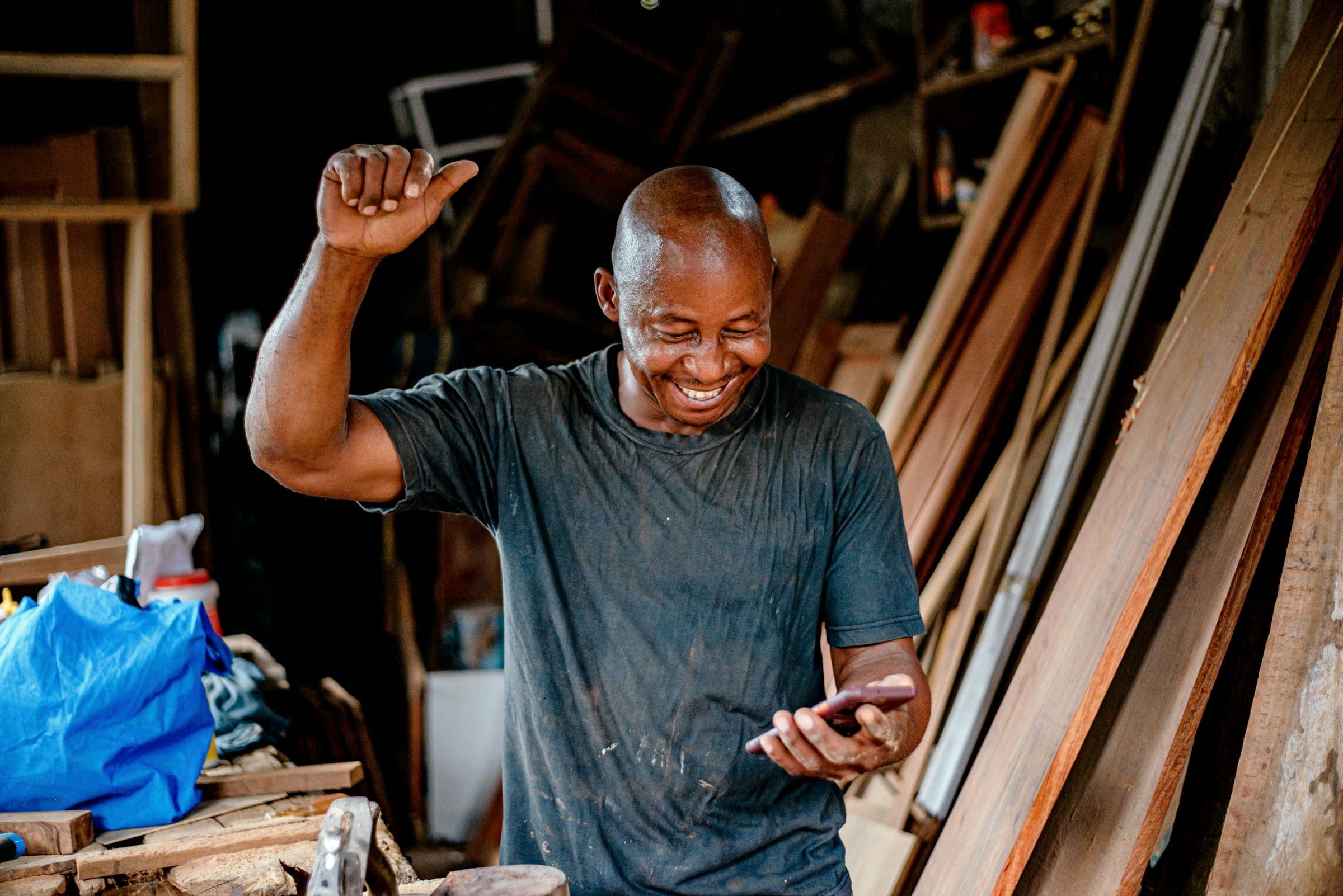 Carpenter in his workshop smiles and raises a fist while looking at his phone