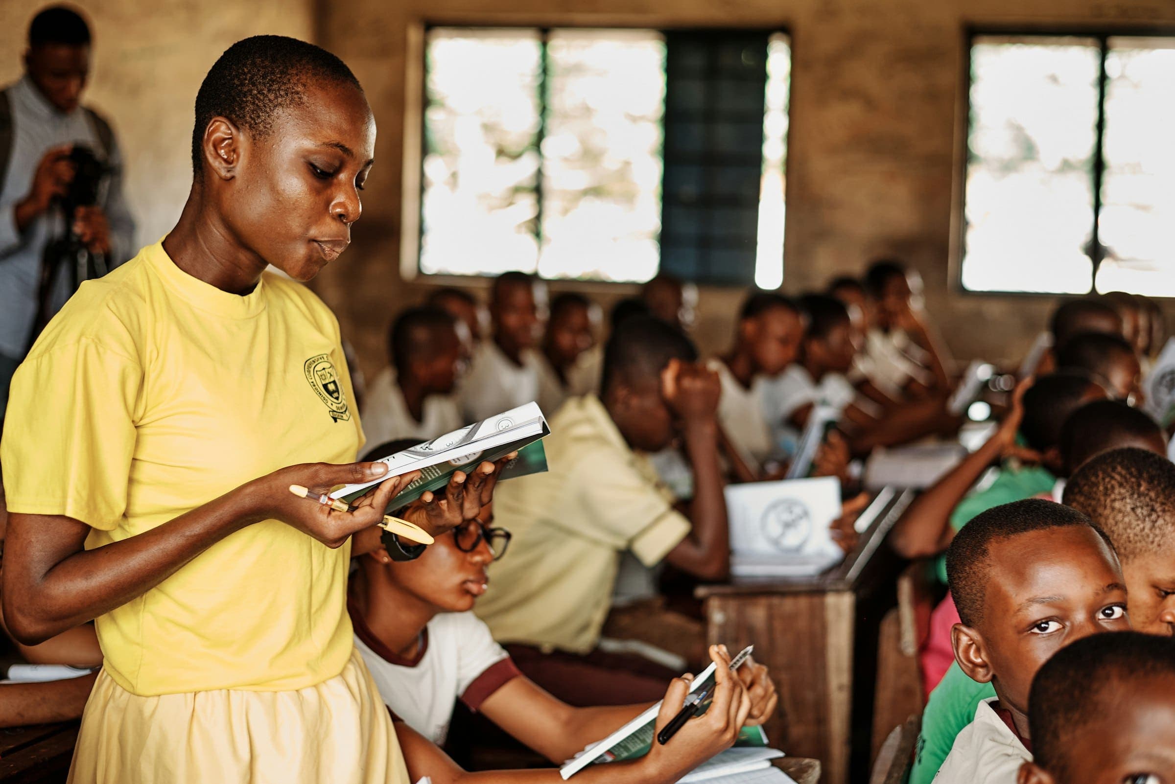 Student in school uniform reads aloud in front of a full classroom