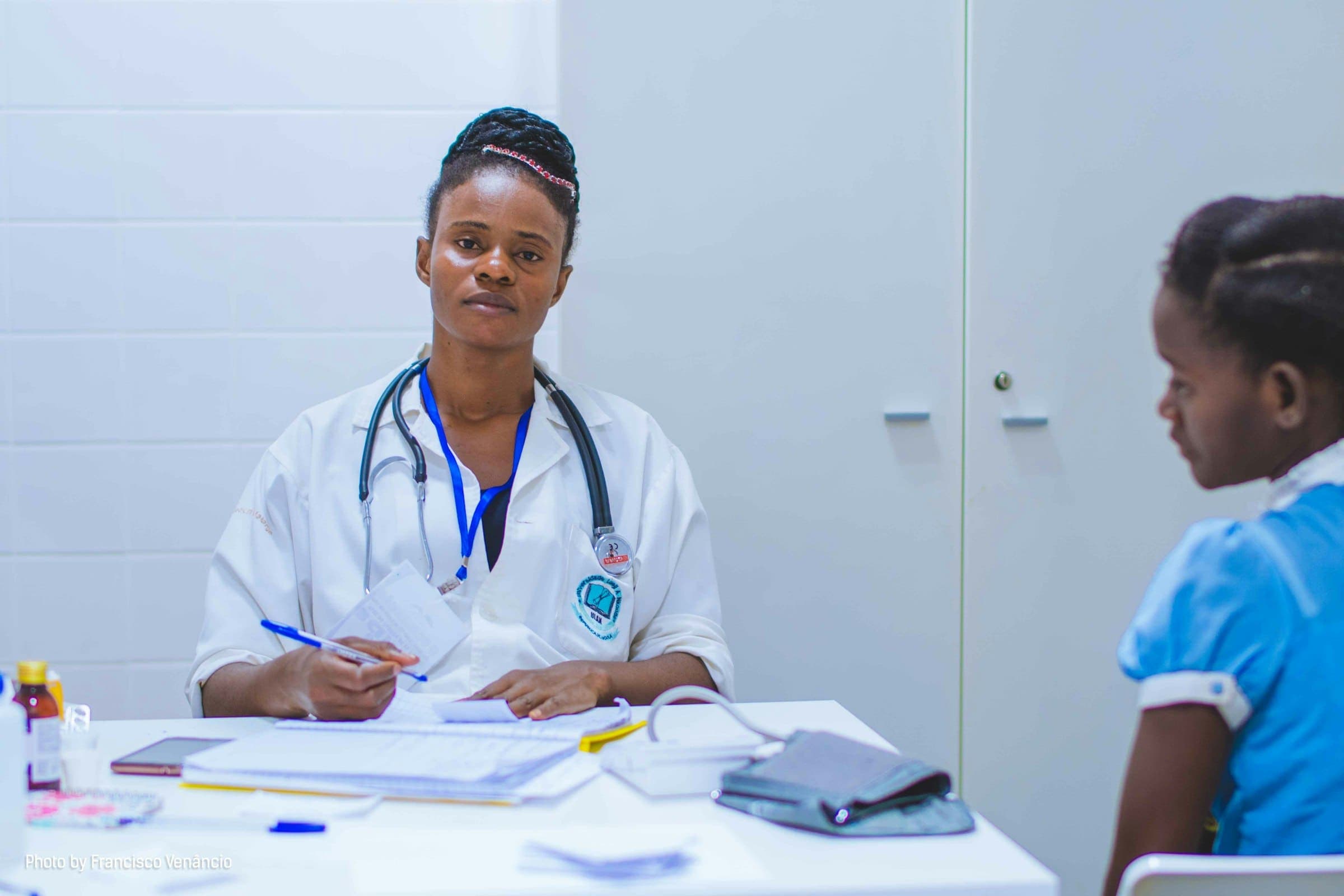 Doctor in a white coat sits at a clinic desk with a young patient