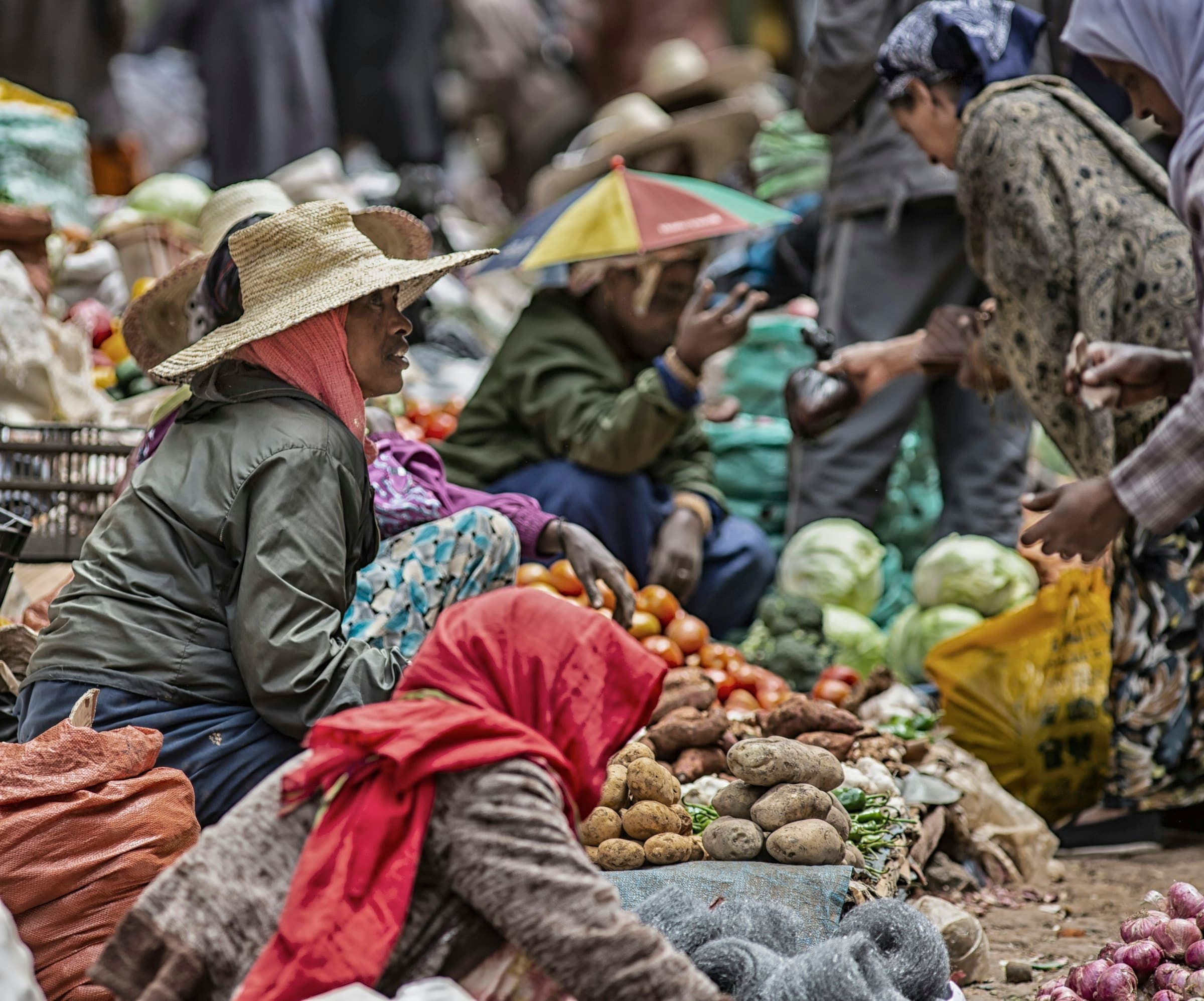 Vendors and shoppers gather around fresh vegetables at a busy open-air market
