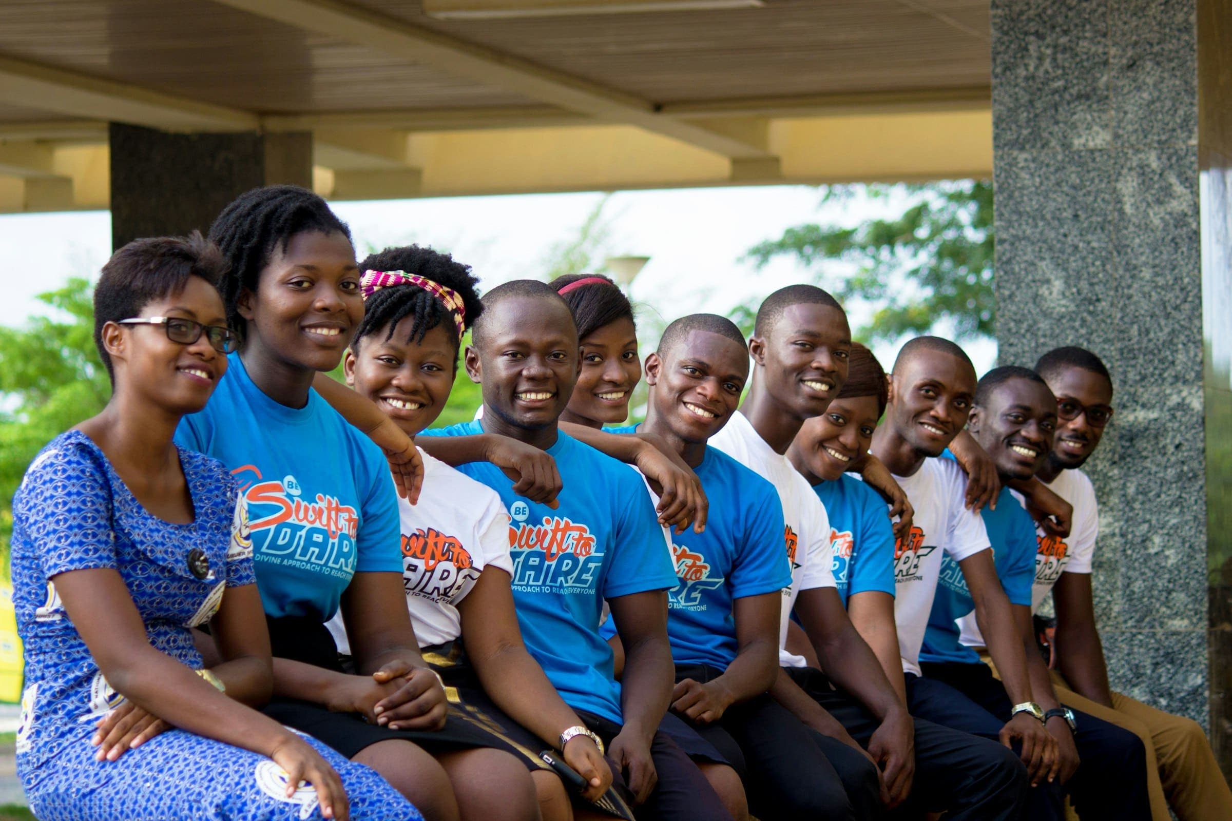 Smiling group of young volunteers in matching T-shirts sits together outdoors